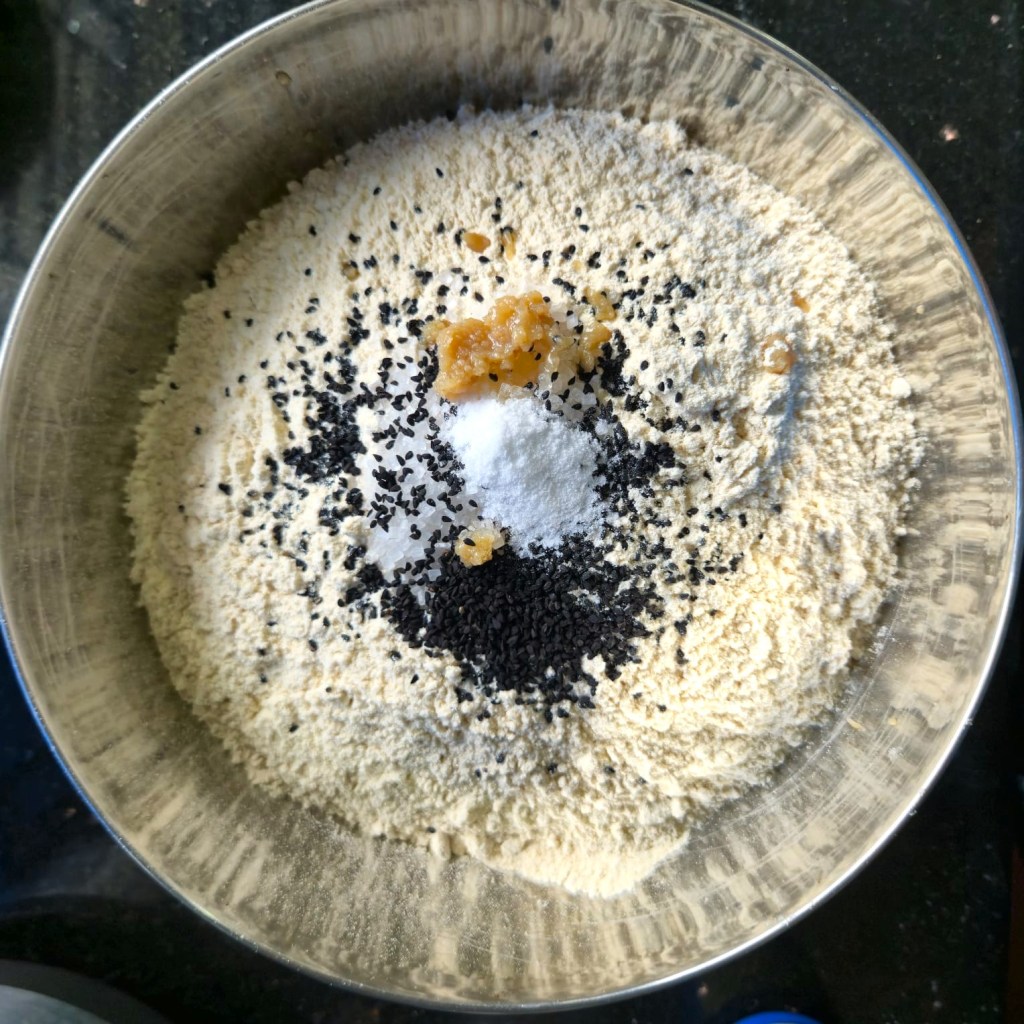 A bowl containing wheat flour, nigella seeds, ghee, salt, sugar, and baking soda