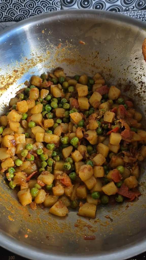 A potato and green peas curry being cooked in a pan