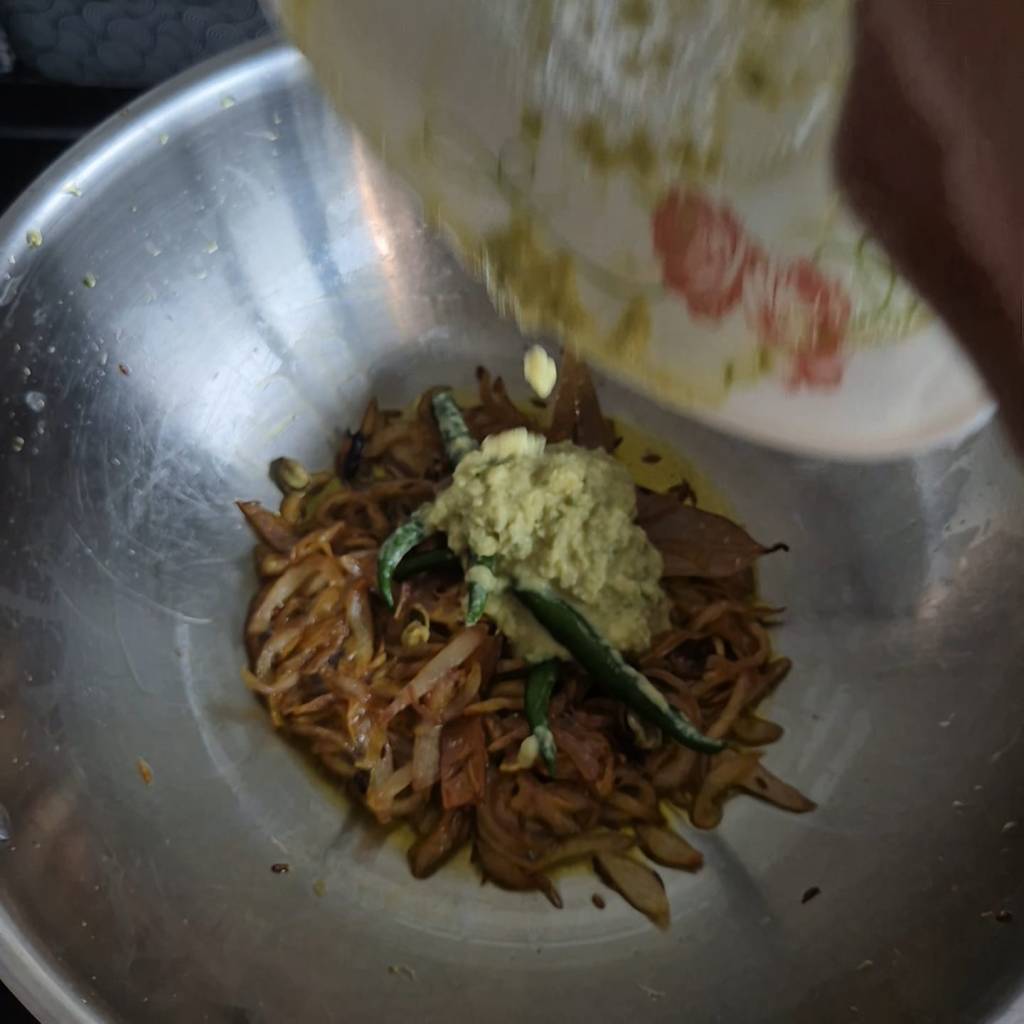 Adding ginger-garlic paste to fried onions in a pan