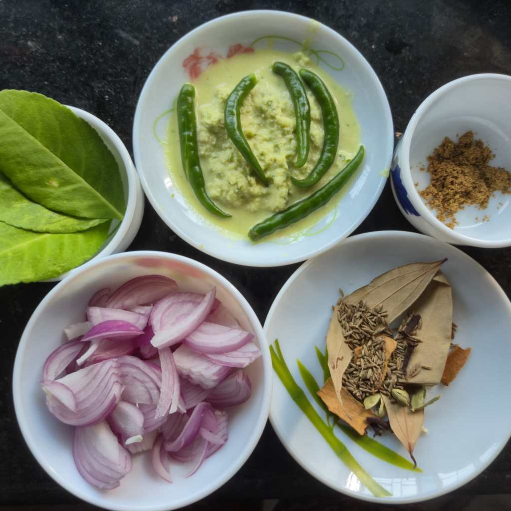 Ingredients for Gondhoraj chicken, which includes lime leaves, sliced onions, whole spices, cumin powder, green chilies, and ginger-garlic paste